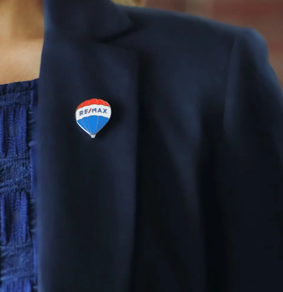 Pin del globo de RE/MAX en el saco de una asesora inmobiliaria